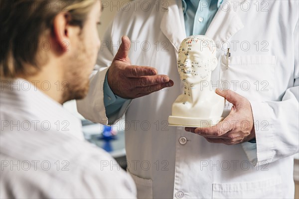 Caucasian acupuncturist showing patient carved bust with diagram