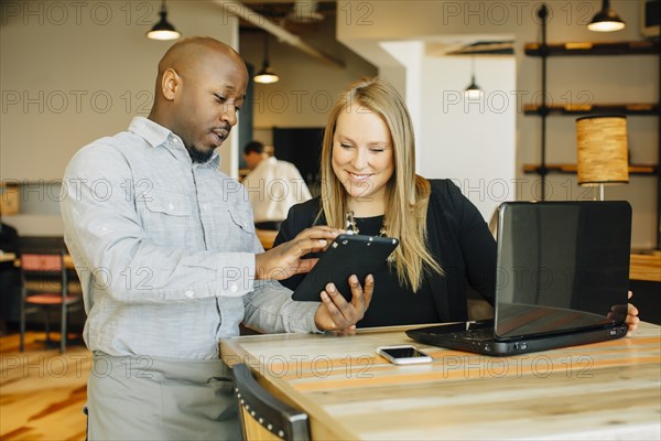 Barista and businesswoman using technology in cafe