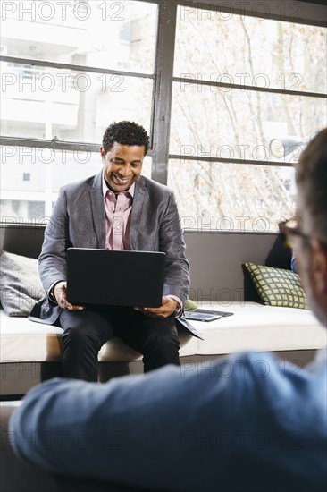 Businessmen using laptop in office lobby