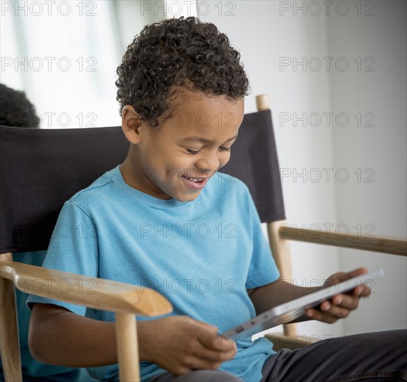 Mixed race boy using digital tablet in directors s chair