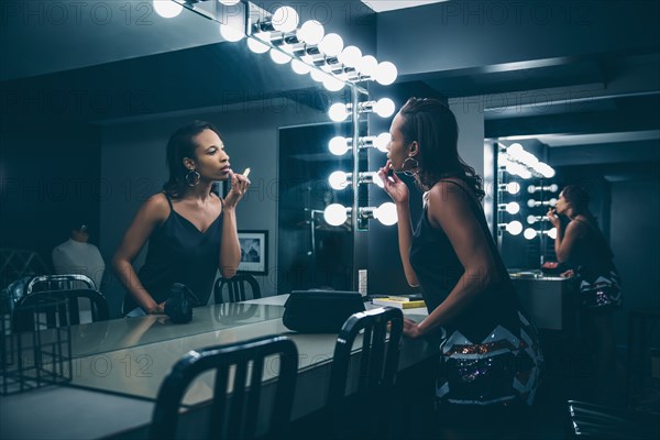 Black woman applying makeup in vanity mirror