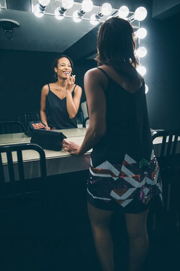 Black woman applying makeup in vanity mirror