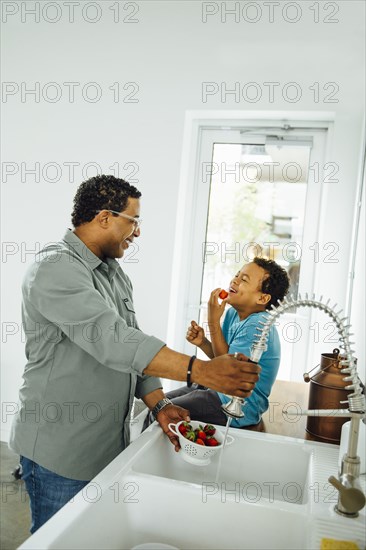 Father and son washing strawberries in kitchen sink