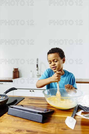 Mixed race boy cooking breakfast with digital tablet in kitchen