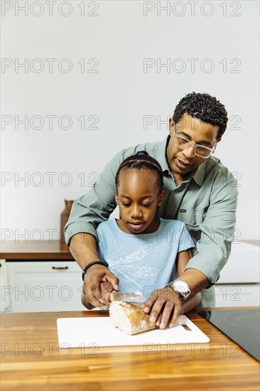 Father teaching daughter to slice bread in kitchen