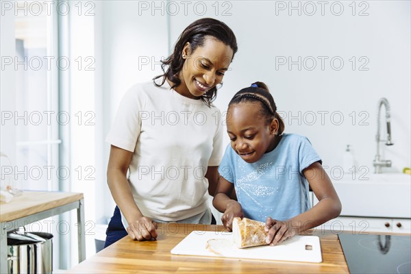 Black mother and daughter slicing bread in kitchen