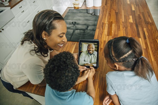 Mother and children video chatting with father in kitchen