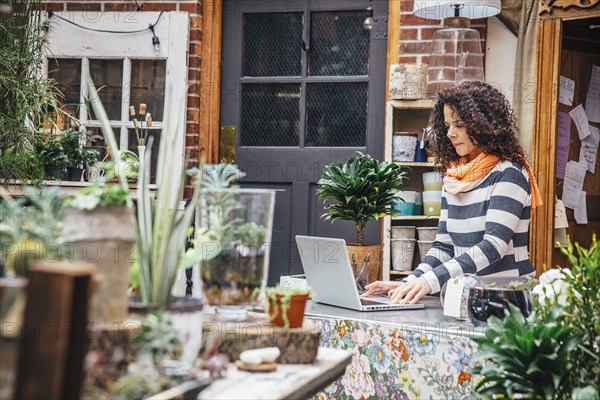 Mixed race employee using laptop in plant nursery