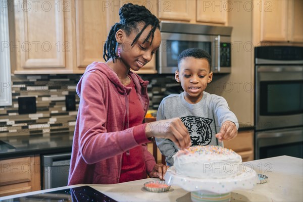 Black brother and sister decorating cake in kitchen