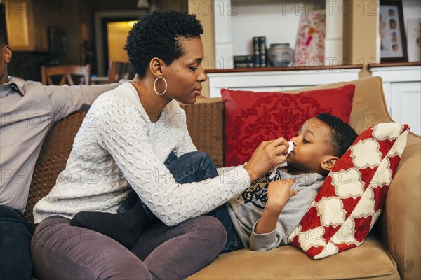 Black woman wiping nose of son on sofa