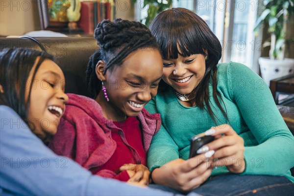 Black sisters using cell phone on sofa