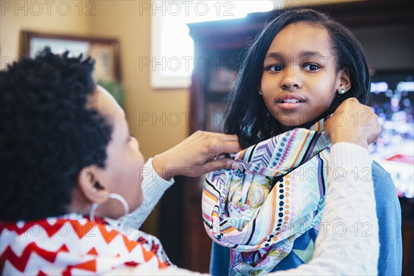 Black mother arranging scarf of daughter