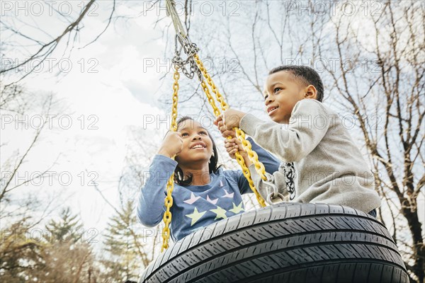 Black brother and sister playing on tire swing