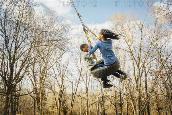 Black brother and sister playing on tire swing