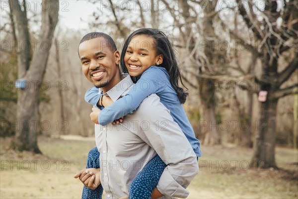 Black father carrying daughter piggyback outdoors