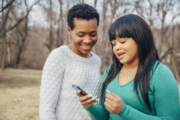 Black mother and daughter using cell phone outdoors