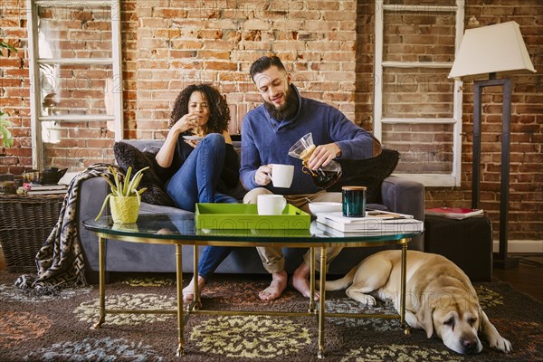 Couple enjoying breakfast on sofa in living room