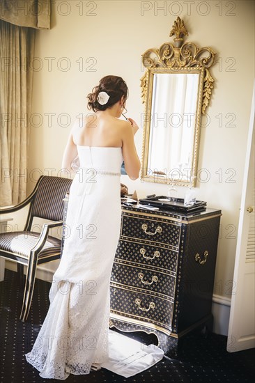 Caucasian bride applying makeup in mirror