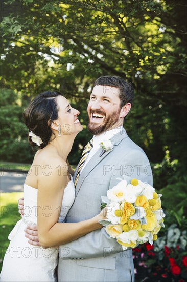 Caucasian bride and groom hugging in garden