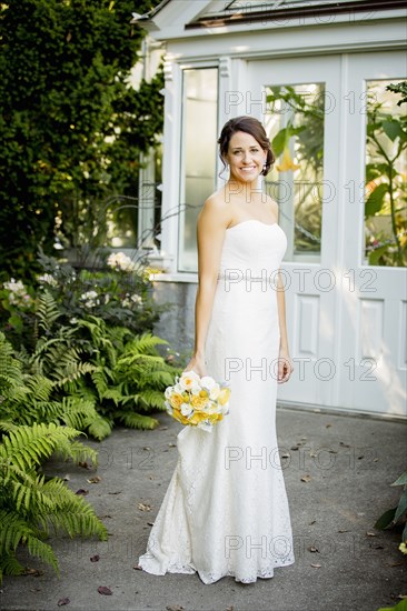 Caucasian bride holding bouquet in garden
