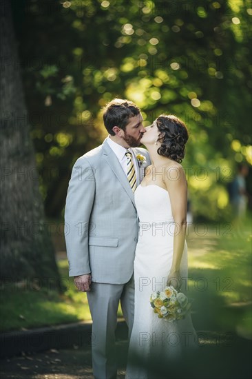 Caucasian bride and groom kissing on rural road