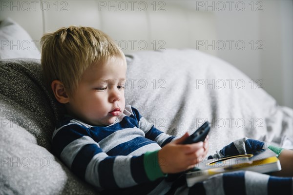 Mixed race boy playing with cell phone on bed