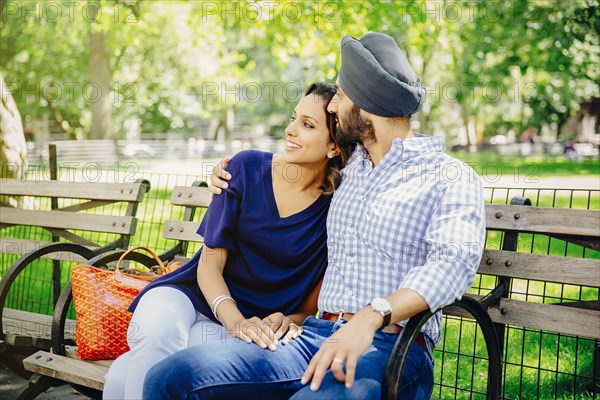 Indian couple hugging on bench in urban park