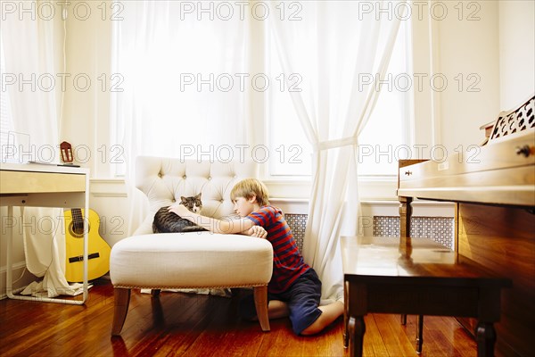 Caucasian boy petting cat in living room