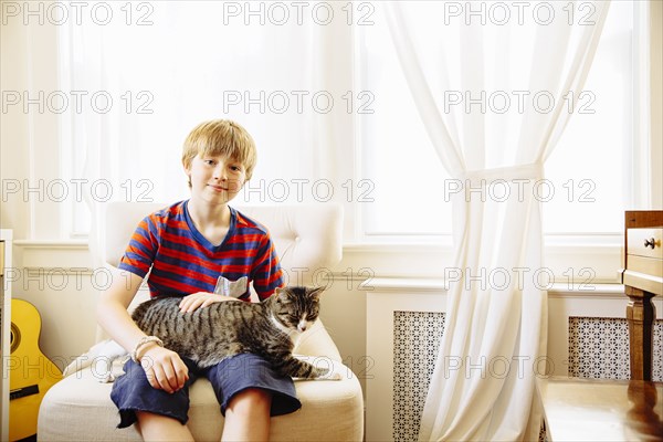 Caucasian boy petting cat in living room