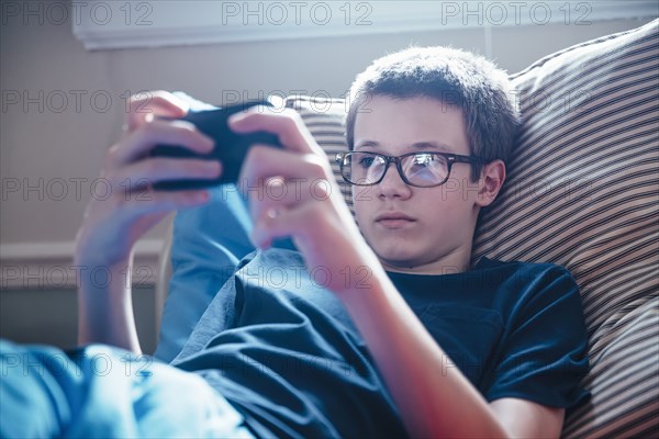 Caucasian boy using cell phone on bed