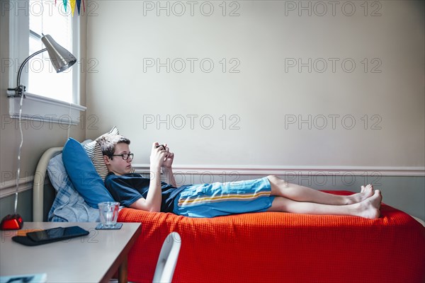 Caucasian boy using cell phone on bed