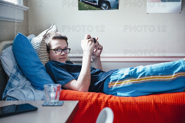 Caucasian boy using cell phone on bed