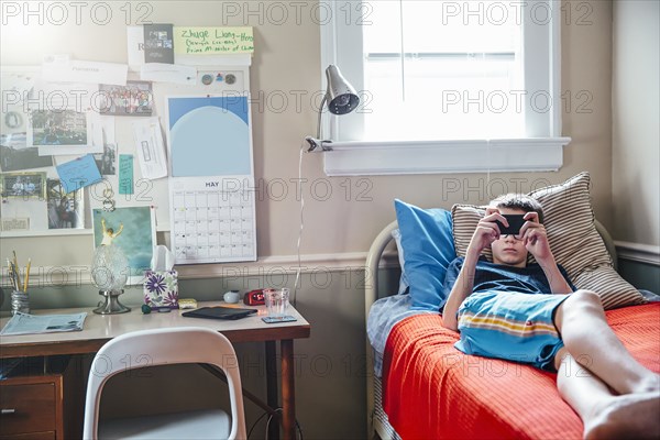 Caucasian boy using cell phone on bed