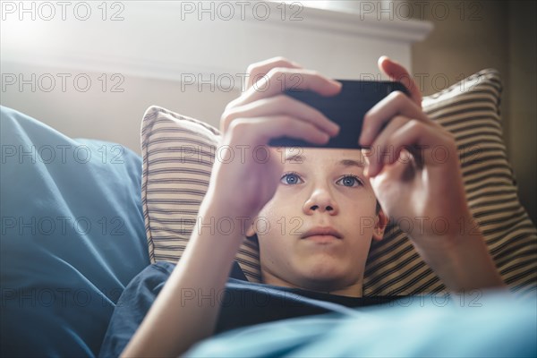 Caucasian boy using cell phone on bed