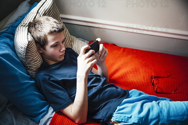 Caucasian boy using cell phone on bed