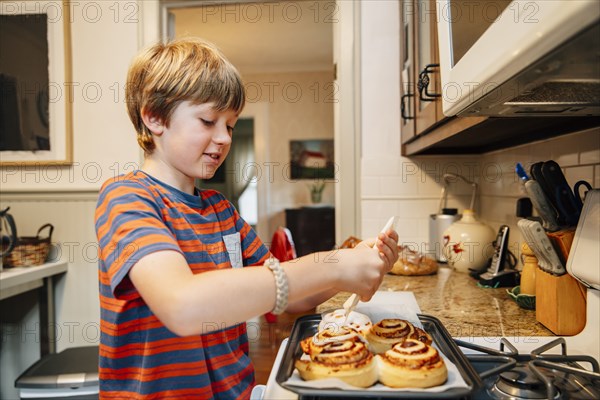 Caucasian boy frosting cinnamon rolls in kitchen