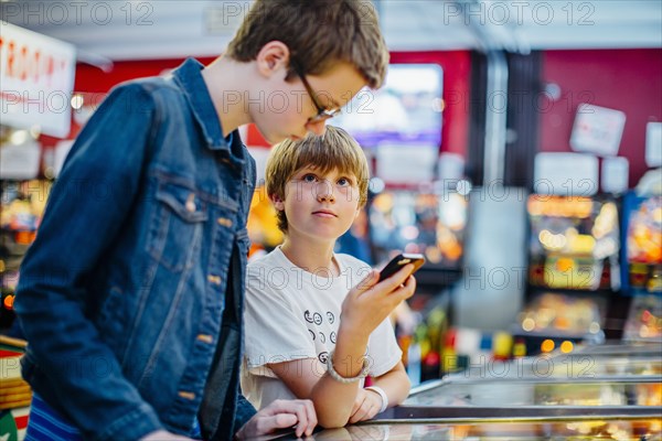 Caucasian brothers using cell phone in arcade