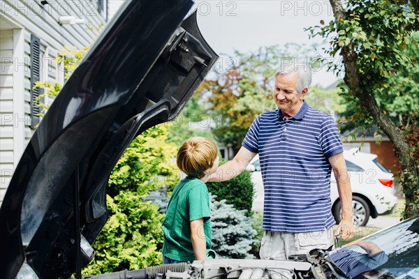 Caucasian grandfather and grandson repairing car in driveway