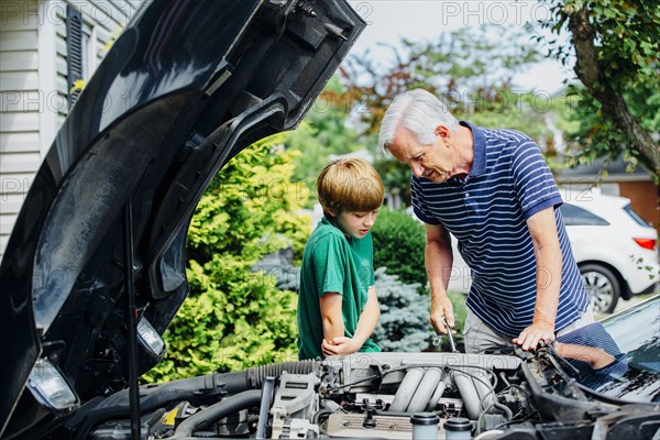 Caucasian grandfather and grandson working on car in driveway