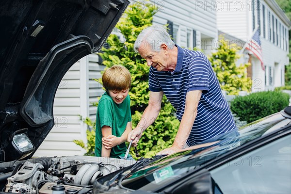 Caucasian grandfather and grandson working on car in driveway