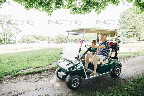 Caucasian grandfather and grandson driving golf cart on course