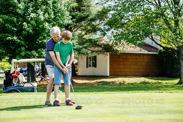 Caucasian grandfather teaching grandson golf on course