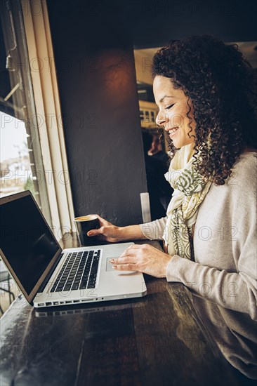 Woman using laptop and drinking coffee in cafe