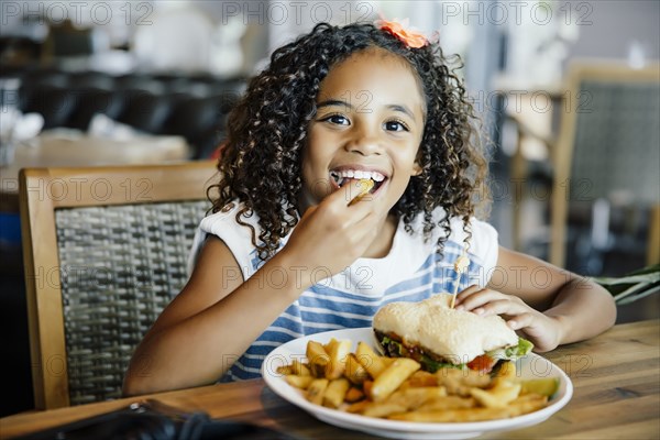 Mixed race girl eating sandwich at table