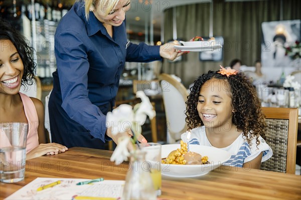 Server bringing birthday dessert to girl in restaurant