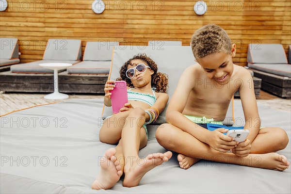 Mixed race children taking selfie with cell phones on patio