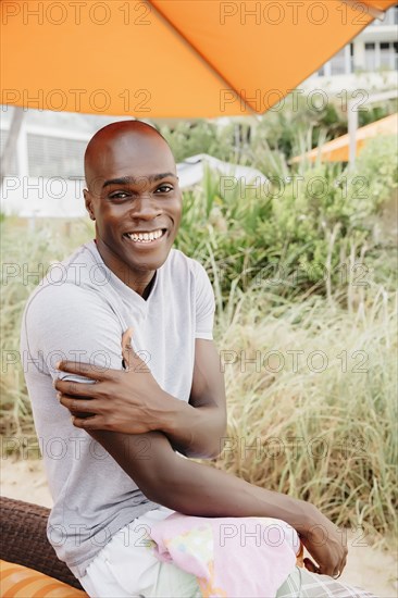 Black man sitting under umbrella on beach