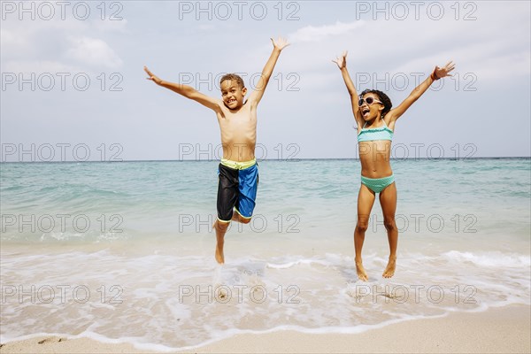 Mixed race children jumping for joy on beach