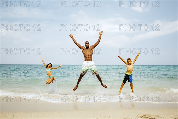 Father and children jumping for joy on beach