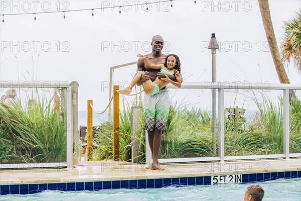 Father carrying daughter into swimming pool